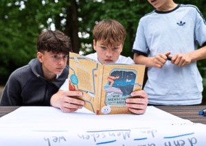 Das Editorial-Bild zeigt drei Schüler beim Testen eines Materials des Rucksack voll Meer. Hier begutachten sie das Buch Wir Menschen und das Meer.